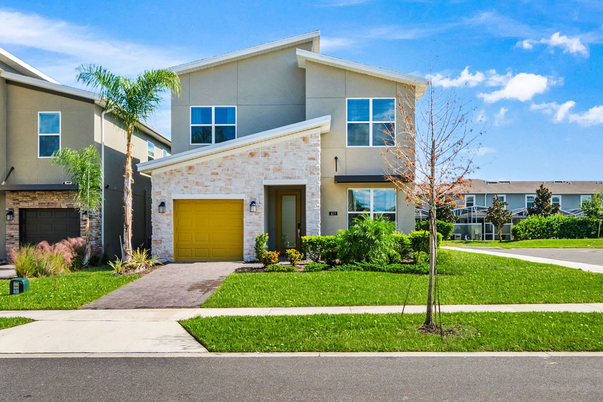 A modern two-story house with a stone facade, a yellow garage door, and a well-maintained lawn.