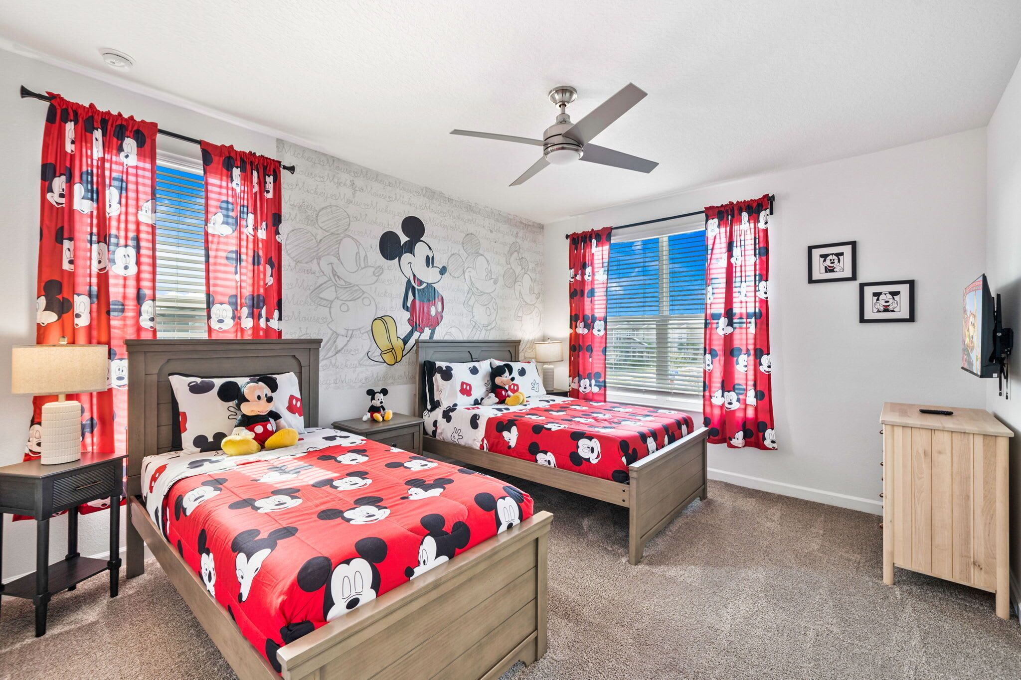 A hotel room with two beds, each with Mickey Mouse themed bedding, a ceiling fan, and Mickey Mouse wall art.