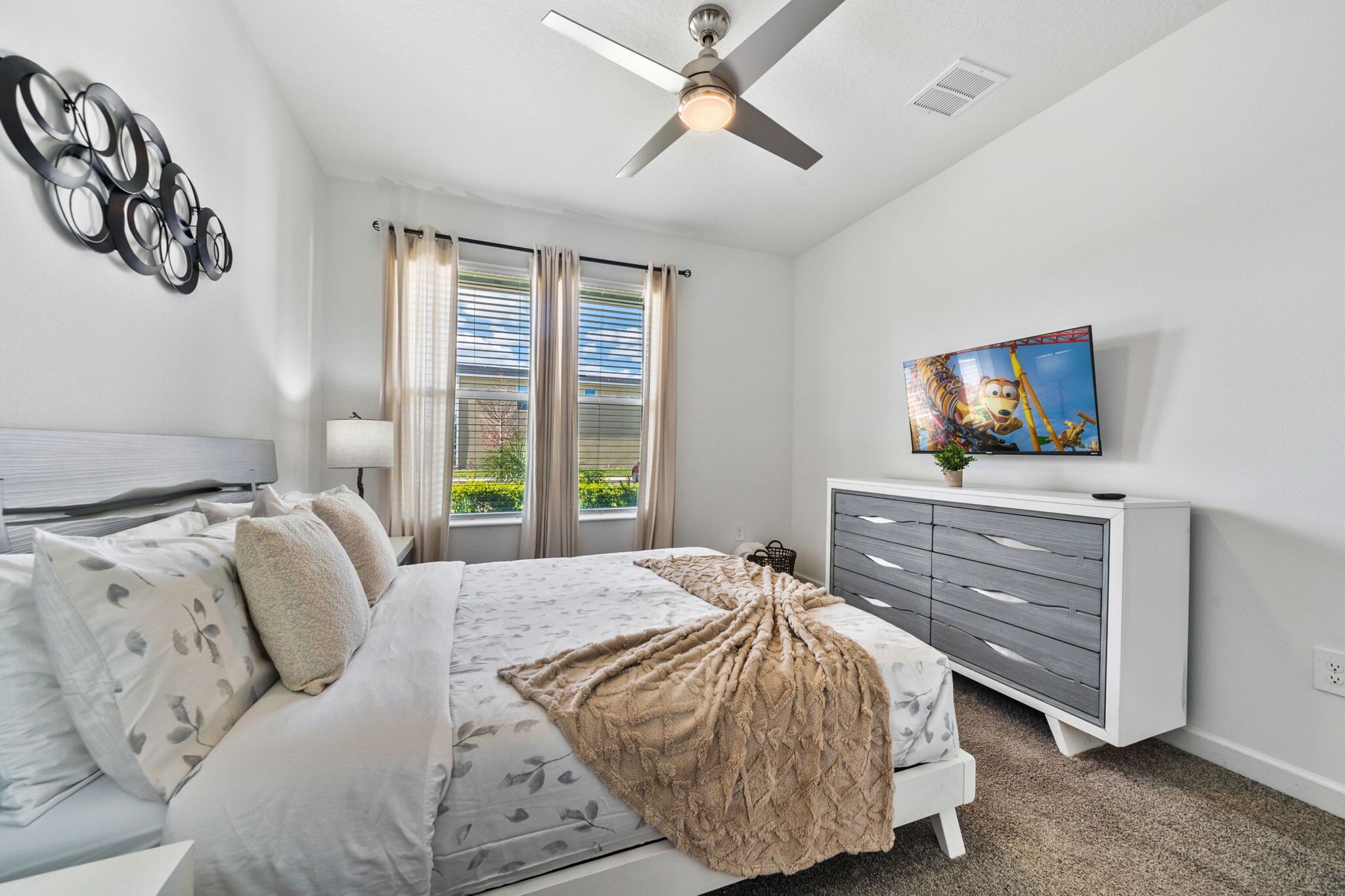 A bedroom with a bed, a ceiling fan, a TV, and a dresser.
