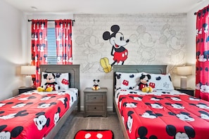 Une chambre avec deux lits, chacun agrémenté de linge de lit sur le thème de Mickey Mouse, d’un autocollant mural représentant Mickey Mouse et de rideaux assortis.