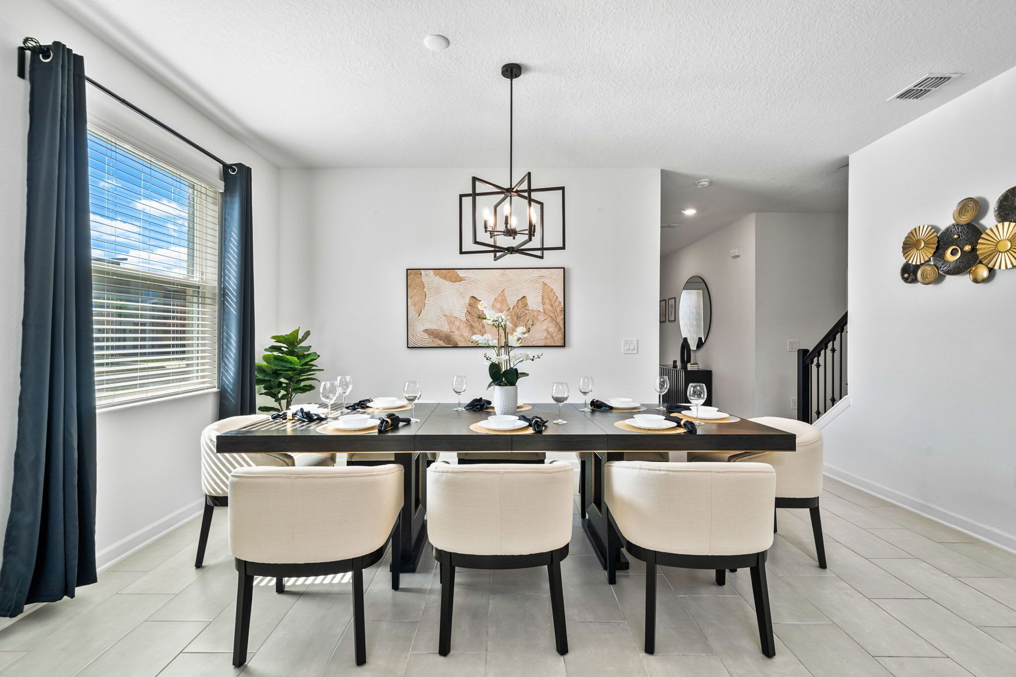 A dining room with a rectangular table set for six, surrounded by six chairs, a chandelier, and a large abstract painting on the wall.