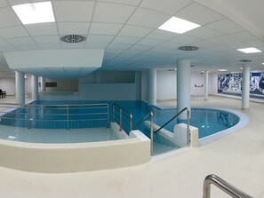 Una piscina interior con una escalera central y un mural en la pared.