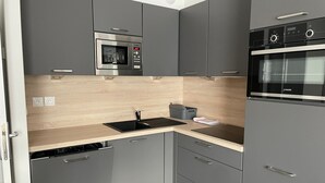 Una cocina moderna con gabinetes grises, un microondas de acero inoxidable, un horno empotrado y un lavamanos negro.