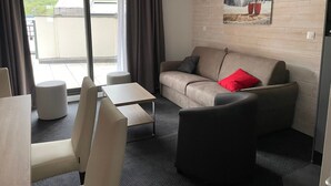 Una camera d'albergo moderna con divano, poltrone, un tavolino e un'ampia finestra che si affaccia su un paesaggio verde.