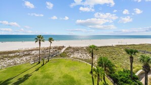 A beach view with a grassy area, palm trees, and a pathway leading to the beach. - Summer House 406B (Orange Beach)