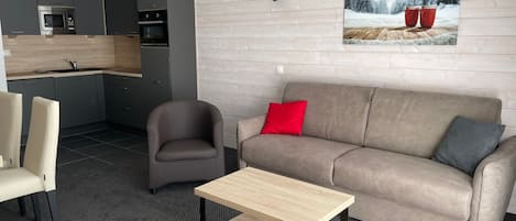 A modern living room with a grey sofa, a wooden coffee table, and a kitchen in the background.