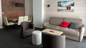 A modern living room with a grey sofa, a round ottoman, a dining table with chairs, and a brick wall. - Gourette: Apartment 6 ppl, 57m², Pets allowed, Pool (Gourette)
