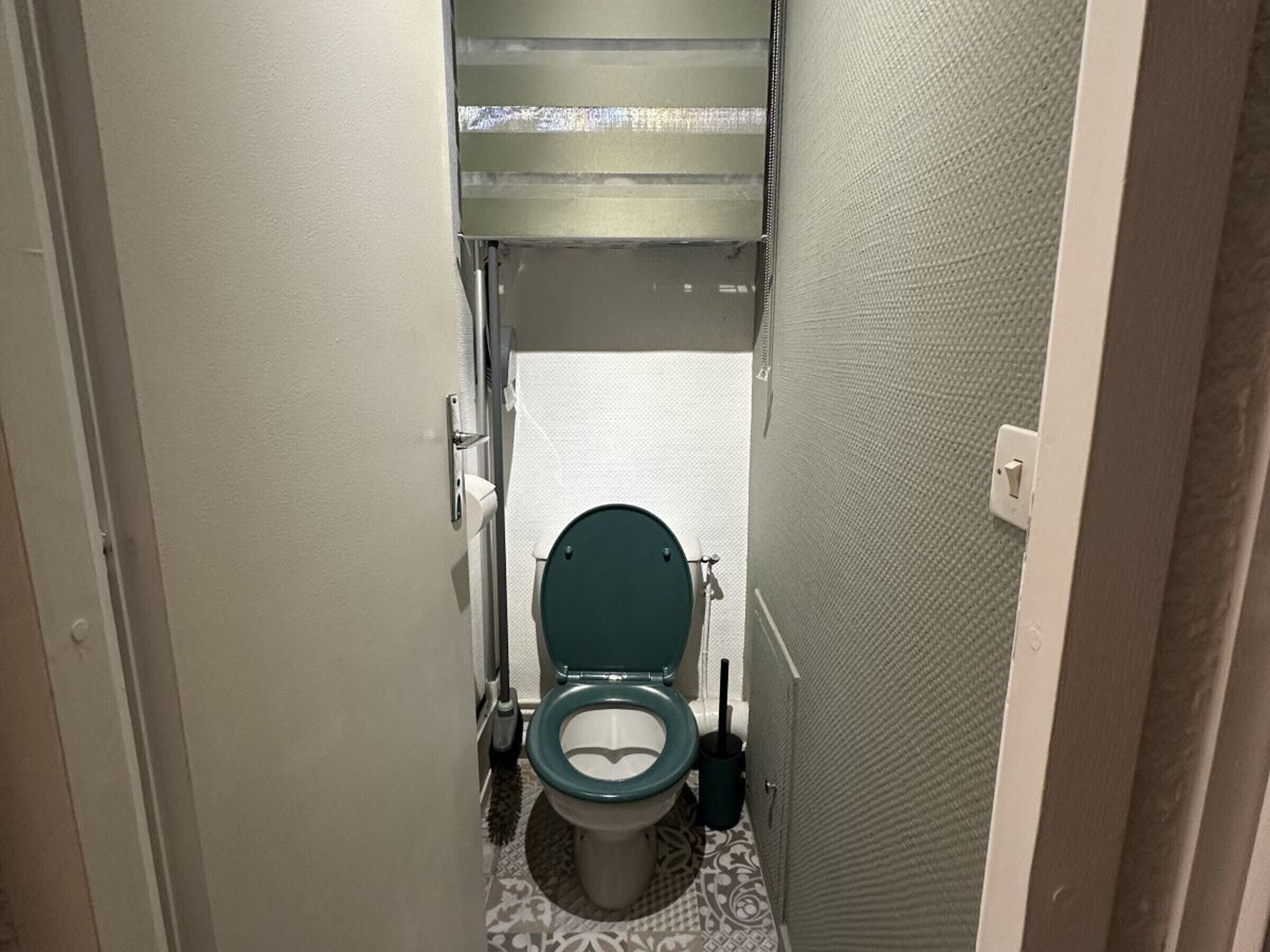 Une petite salle de bain comprenant des toilettes, une brosse à récurer et un porte-rouleau de papier toilette.