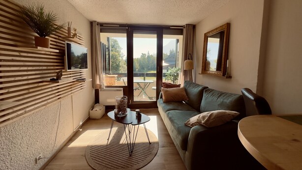 Een gezellige woonkamer met een bank, een kleine tafel en uitzicht door een glazen deur.