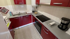 A kitchen with red cabinets, a sink, a stove, and a coffee maker. - Spacious T2 with balcony near slopes in Le Lioran (Le Lioran)