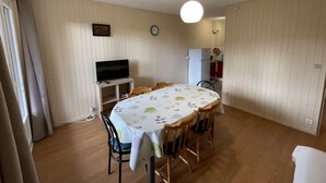 A dining area with a round table, chairs, a television on a stand, a clock, and a kitchen in the background. - Spacious T2 with balcony near slopes in Le Lioran (Le Lioran)