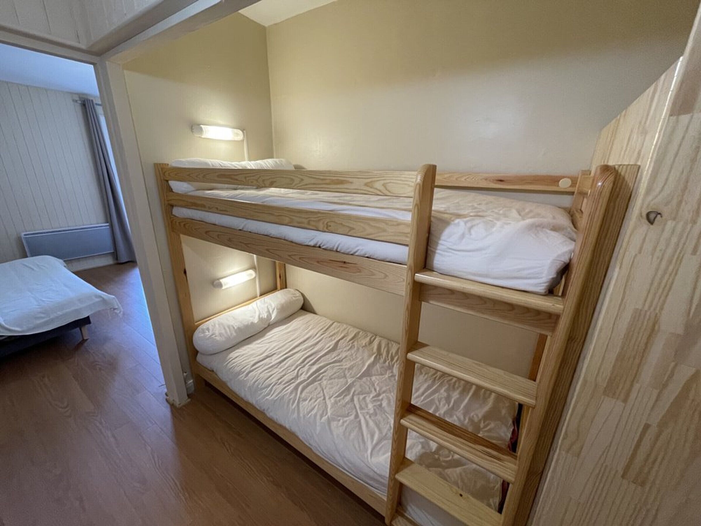 Habitación con literas de madera, un estante pequeño y una mesita de noche.