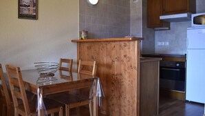 Een compacte keuken met houten kastjes, een witte koelkast, en een eethoek met een houten tafel en stoelen.