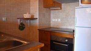 Een keuken met houten kastjes, een roestvrijstalen spoelbak, een oven en een witte koelkast.