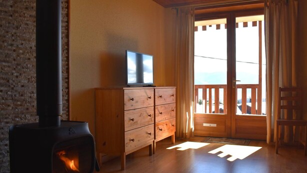 Een knus verblijf met een houtkachel, een houten dressoir, een televisie en een balkon met uitzicht.