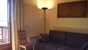 Een woonkamer met een donkergrijze bank, een houten stoel, een vloerlamp en een schilderij aan de muur.
