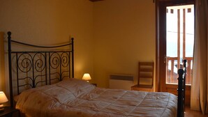 Een slaapkamer met een bed, nachtkastje, lamp, stoel en een raam met gordijnen.