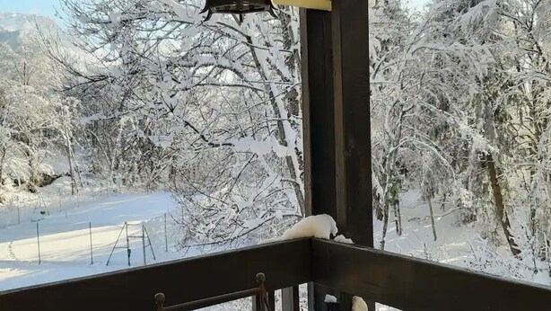 Een balkon bedekt met sneeuw, met uitzicht op een besneeuwd landschap en bomen.