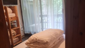 Een slaapkamer met een bed, een houten plankunit en een raam met dunne gordijnen.