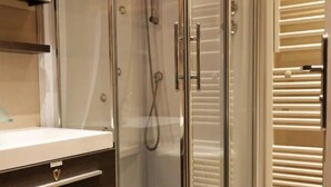 Een moderne badkamer met een glazen douchecabine, een wit wastafelmeubel en een donker houten kast.