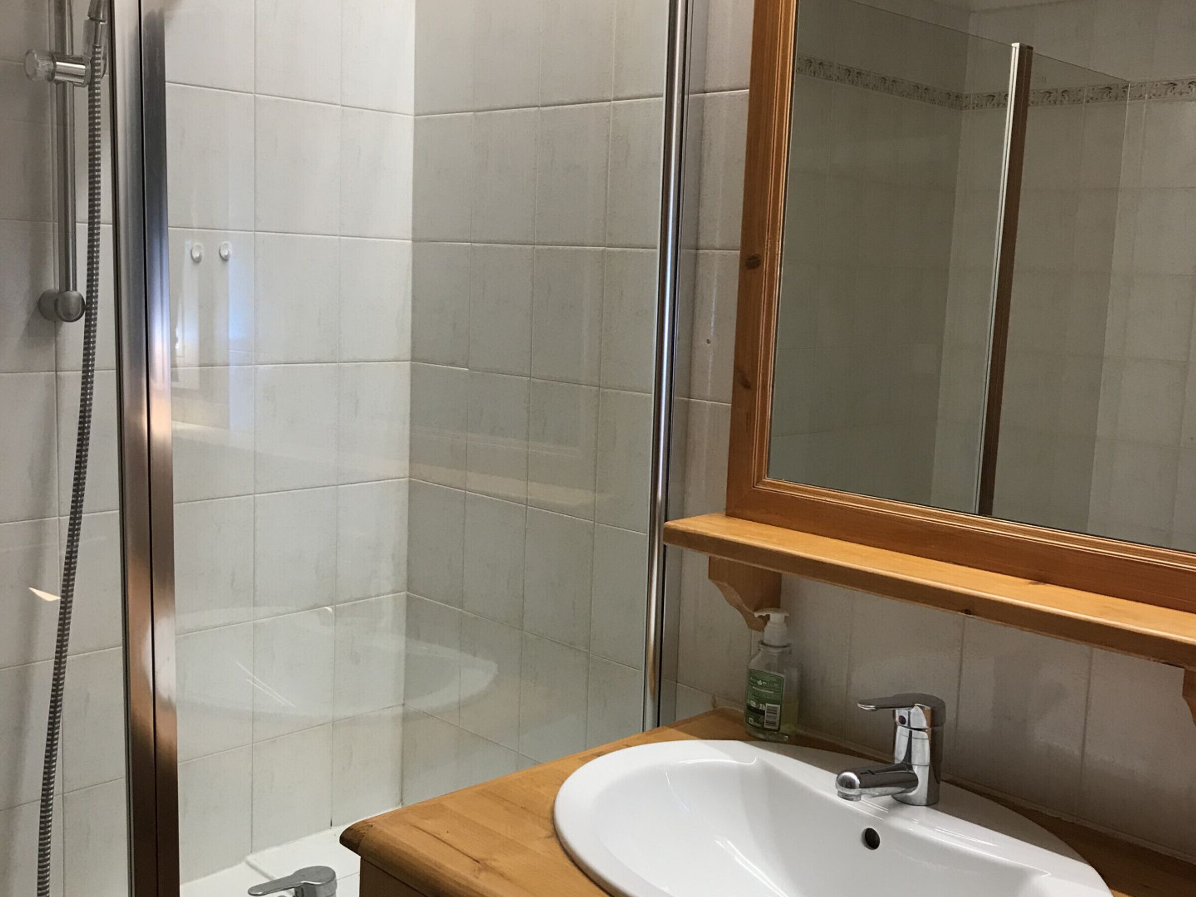 Une salle de bain avec une douche à parois de verre, un meuble-lavabo en bois, un lavabo blanc et un miroir.