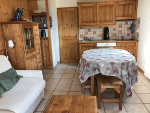Ein gemütlicher Wohnbereich mit einer Holzdirektiva, einem runden Tisch mit gemustertem Tischläufer und einer Küche mit Holzausstattung und einer gefliesten Spritzwand.
