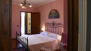 A bedroom with a bed, a chair, a door, and a wall-mounted picture. - Room 'Il Leccio - Podere Del Griccia' with Shared Pool, Wi-Fi and Air Conditioning (Civitella in Val di Chiana)