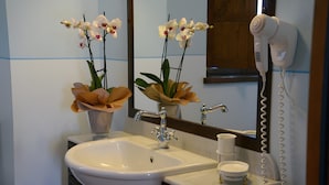 A bathroom with a sink, mirror, hair dryer, and two orchid vases. - Room 'Il Leccio - Podere Del Griccia' with Shared Pool, Wi-Fi and Air Conditioning (Civitella in Val di Chiana)