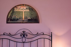 Una obra de arte enmarco que muestra un paisaje con un edificio y árboles, colocada sobre una cama con cabecera decorativa.