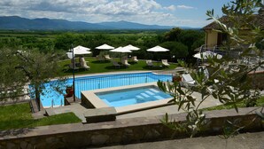 A swimming pool with lounge chairs and umbrellas, surrounded by greenery and mountains in the background. - Room 'Il Leccio - Podere Del Griccia' with Shared Pool, Wi-Fi and Air Conditioning (Civitella in Val di Chiana)