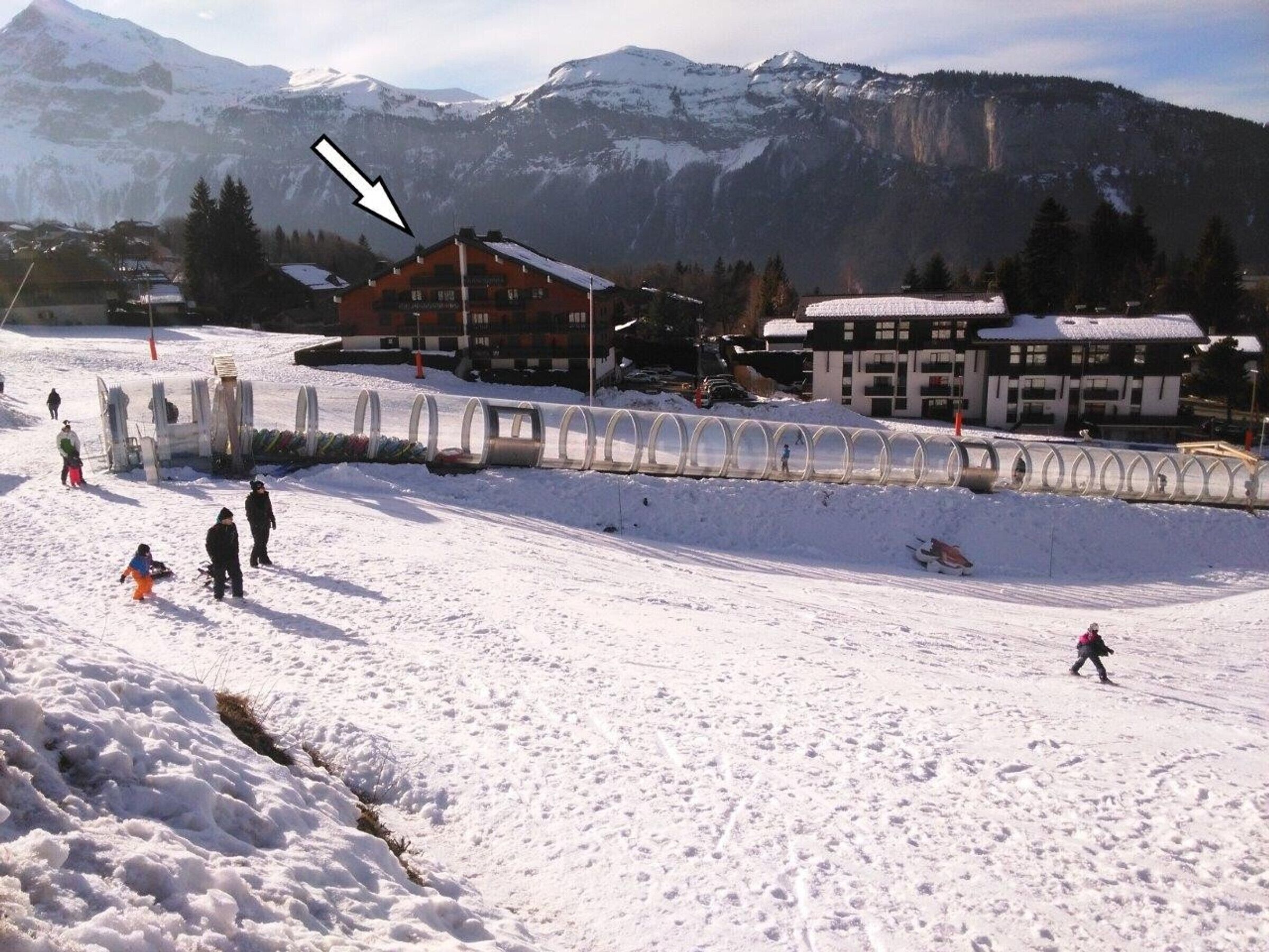 A ski resort with a snow-covered slope, buildings, and a mountain in the background.