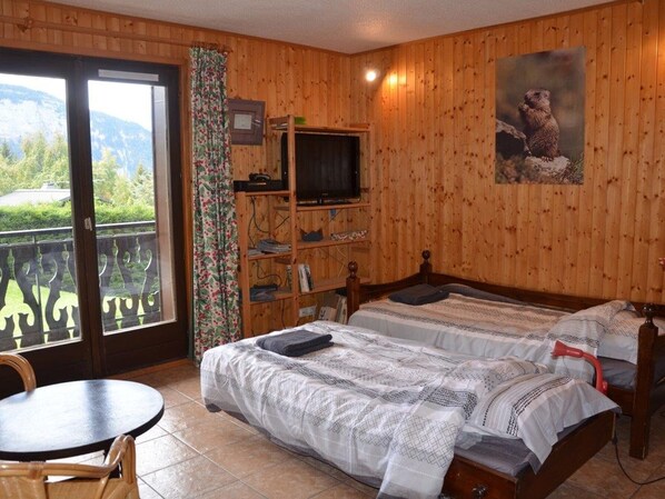A wooden room with a bed, a TV, and a balcony with a view of greenery. - Charming 2-room with WIFI for 4 guests at Le Pernant (Arâches-la-Frasse)