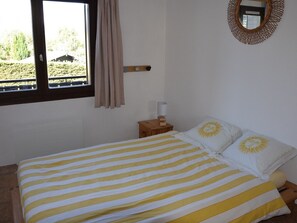 A bedroom with a bed, a nightstand, a lamp, a window with curtains, and a wall-mounted mirror. - Charming 2-room with WIFI for 4 guests at Le Pernant (Arâches-la-Frasse)