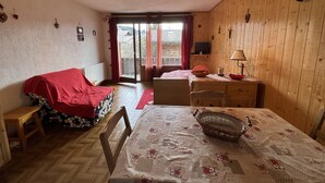 Une pièce confortable avec un lit, une table, une chaise, un téléviseur et une fenêtre avec des rideaux.