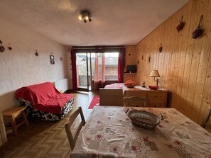 Ein gemütliches Zimmer mit einem Bett, einem Tisch, einem Stuhl, einem Fernseher und einem Fenster mit Vorhängen.