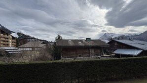 Un bâtiment traditionnel en bois, doté d’un toit en pente, entouré d’une haie et avec une chaîne de montagnes en arrière-plan.