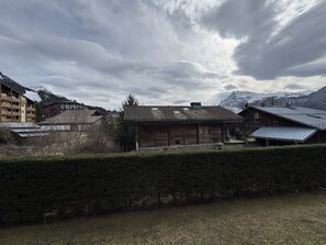 Ein traditionelles Holzhaus mit geneigtem Dach, umgeben von einer Hecke und mit Blick auf eine Berglandschaft.