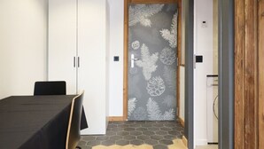Una habitación con una mesa y sillas negras, armarios blancos, una puerta de madera con diseño de pino y un suelo de baldosas hexagonales.