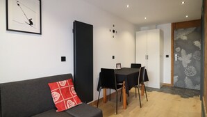 Una sala moderna con un sofá gris, un cojín decorativo rojo estampado, una mesa de comedor con cuatro sillas y una puerta con diseño de piñas.