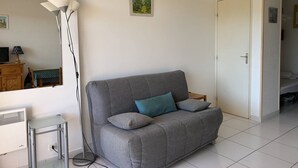 A modern living room with a grey sofa, a small table, a floor lamp, and a white door. - Studio with terrace in Bormes-les-Mimosas (Bormes-les-Mimosas)