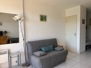 Ein modernes Wohnzimmer mit einem grauen Sofa, einem kleinen Tisch, einer Stehlampe und einer weißen Tür.