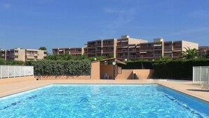 A swimming pool with a clear blue water surface, surrounded by a low fence. In the background, there are multi-story buildings with balconies and a clear sky. - Studio with terrace in Bormes-les-Mimosas (Bormes-les-Mimosas)