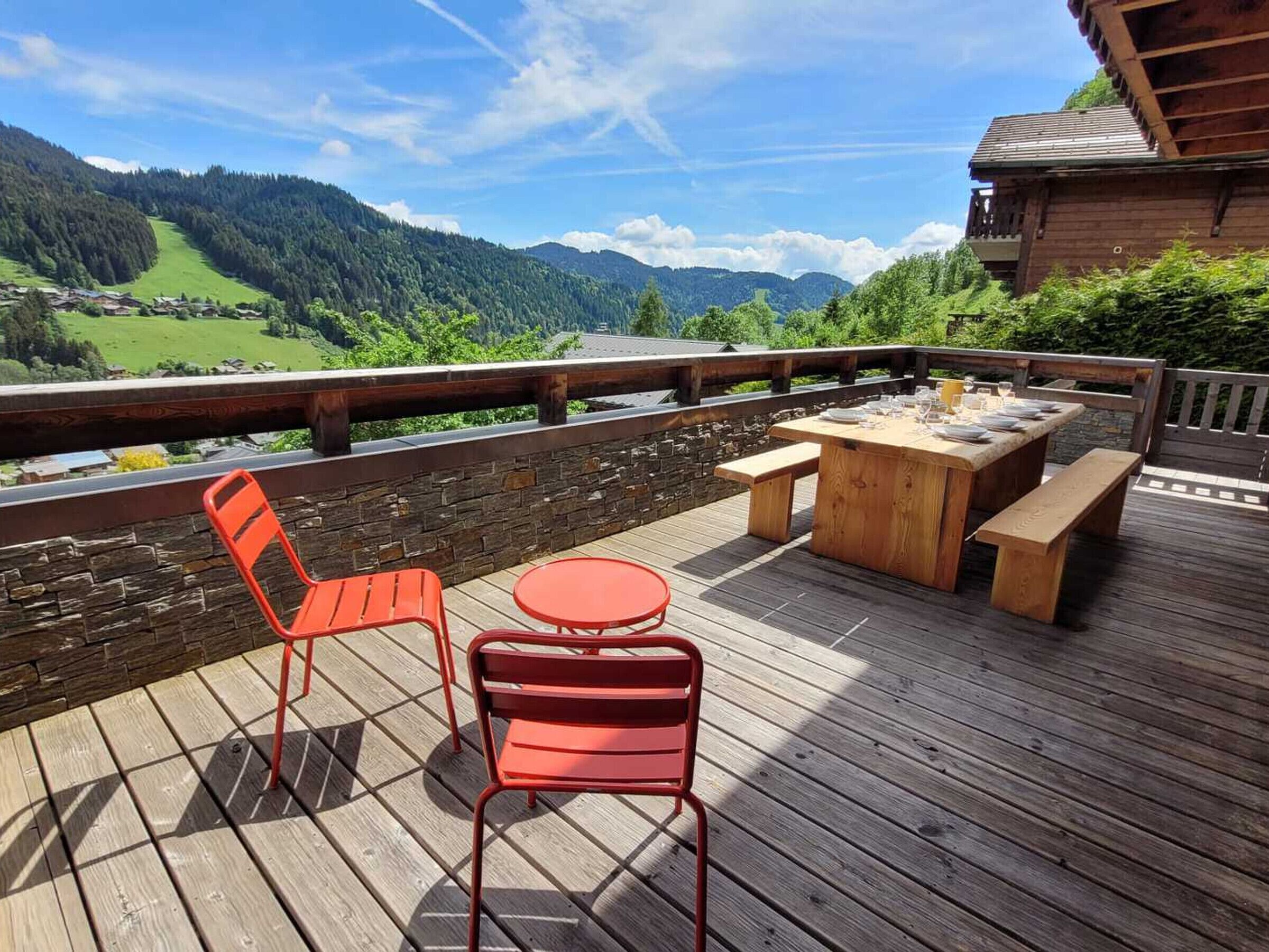 A wooden deck with a table and chairs, overlooking a valley with mountains.