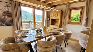 Un'area pranzo con un tavolo in legno apparecchiato per sei persone, circondata da sedie in vimini, un armadietto in legno e vista sulle montagne attraverso ampie finestre.
