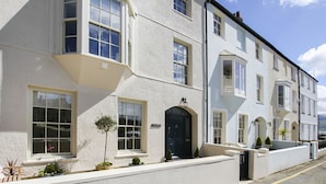 A row of white terraced houses with multiple windows and a small front garden. - Tri Raglan Bach (Beaumaris)
