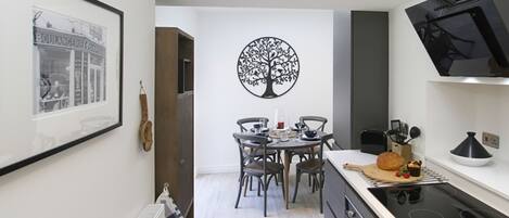 A modern kitchen with a dining area, featuring a black tree wall art, a framed picture, and a black TV on the wall.