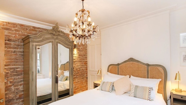 A bedroom with a large bed, a wooden wardrobe, and a chandelier. - Tri Raglan Bach (Beaumaris)