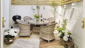 A patio with wicker furniture, a round table, and a grill. - Tri Raglan Bach (Beaumaris)