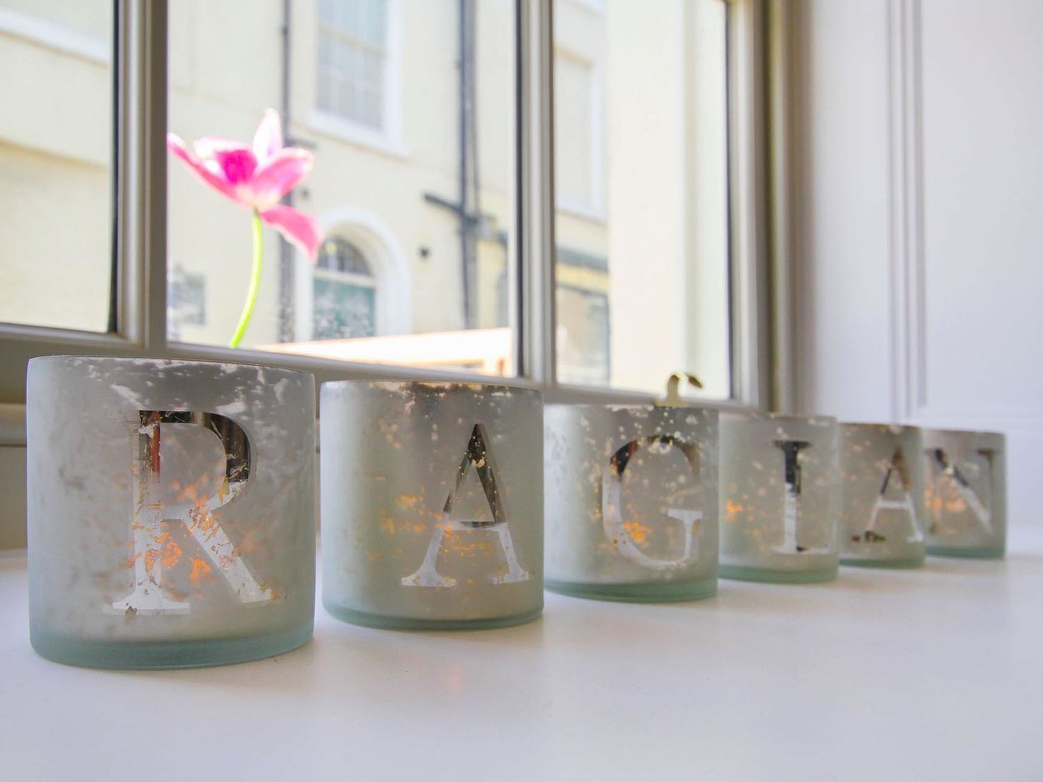 Una fila de candelabros de vidrio esmerilado con la palabra "RAGIAN" sobre un alféizar.
