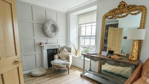 A room with a fireplace, a mirror, a chair, and a wooden floor. - Tri Raglan Mawr (Beaumaris)